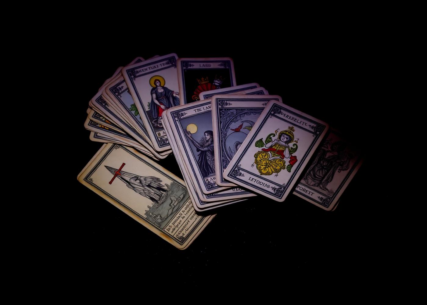 Antique oracle and tarot cards fanned across black velvet in low violet light